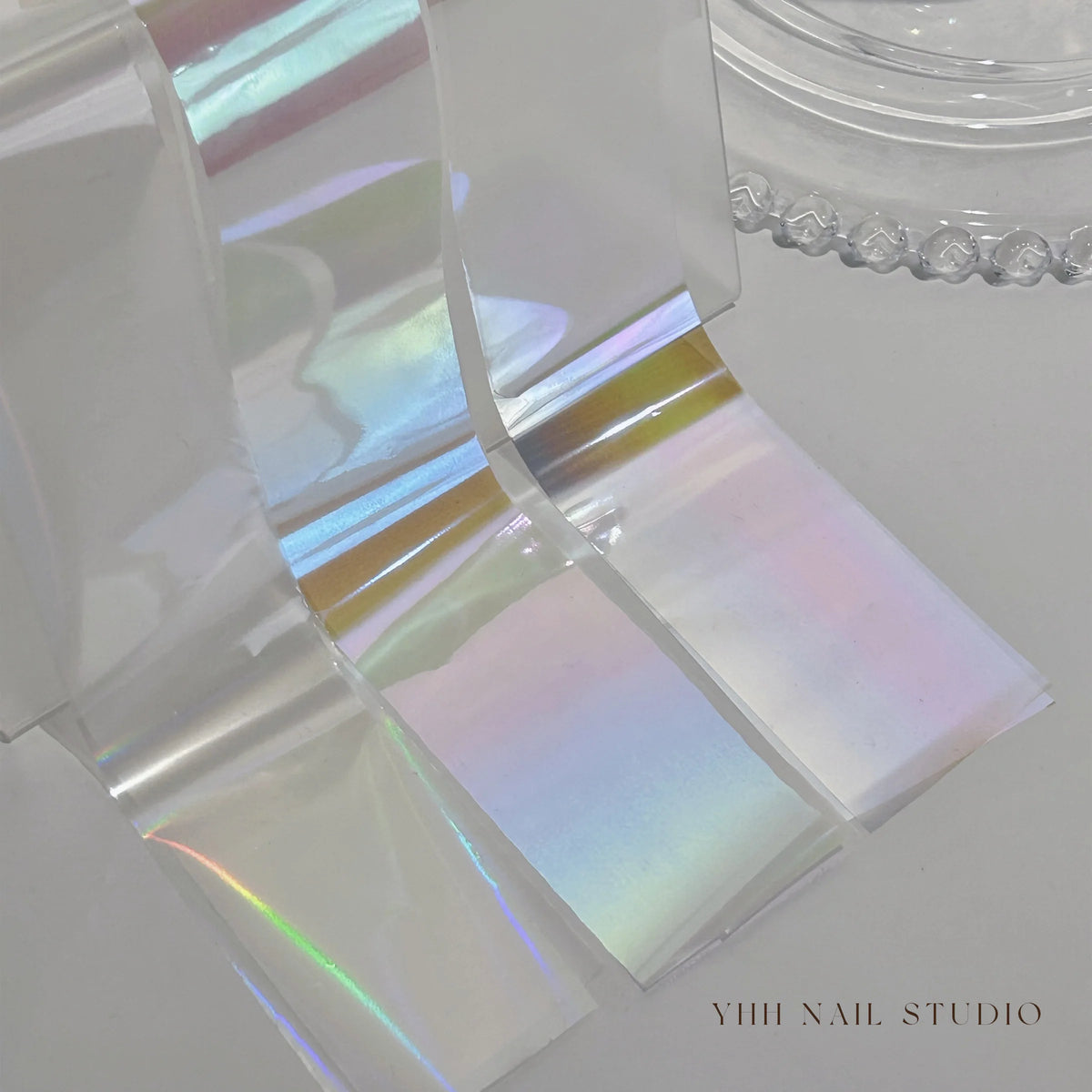 Iridescent YHH aurora transfer foil strips draped beside a glass dish